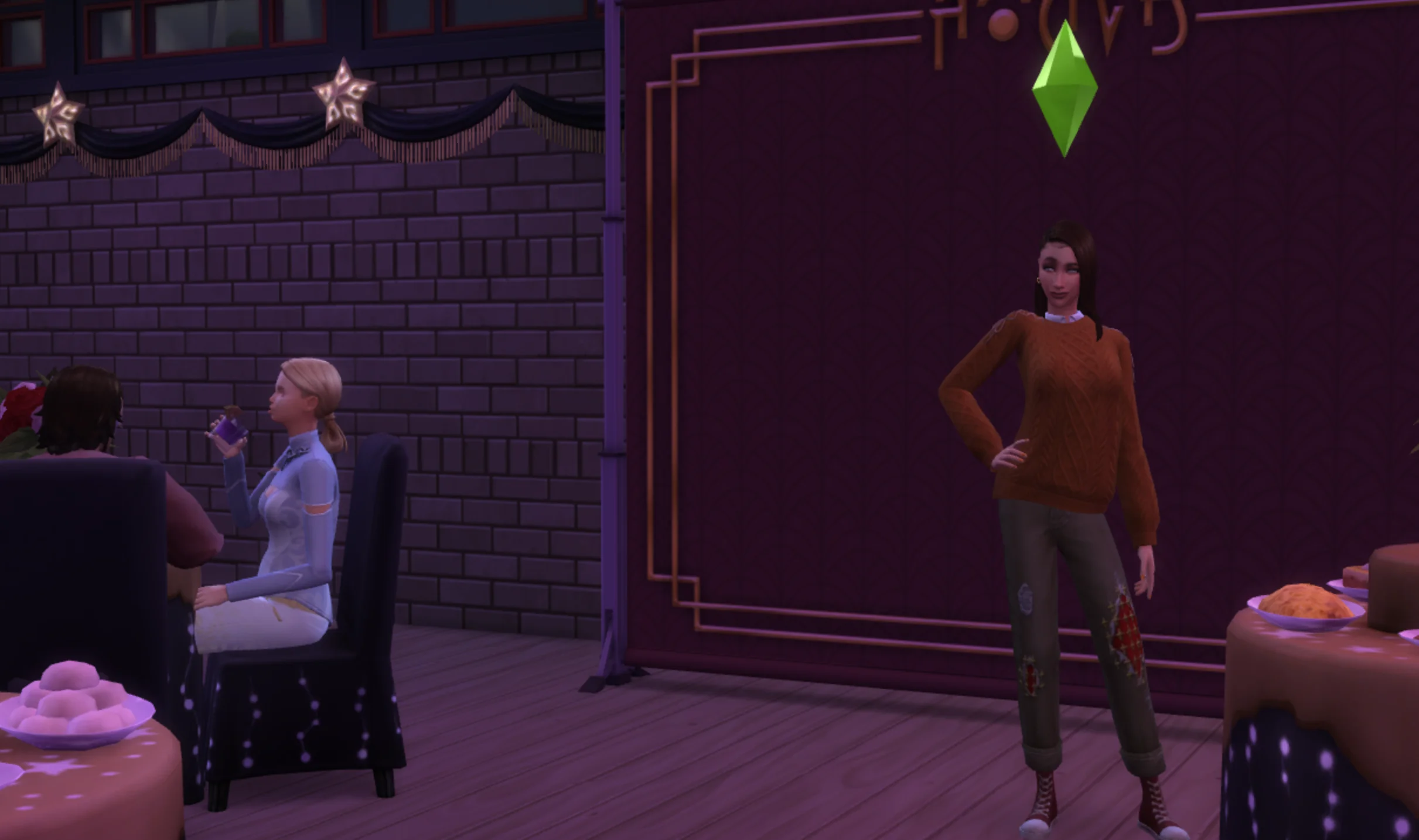 a screenshot from the Sims 4 of a woman with long brown hair, in a brown sweater and black pants posing with her hand on her hip in front of a backdrop while everyone else sits at tables eating food. Nobody's taking her photo