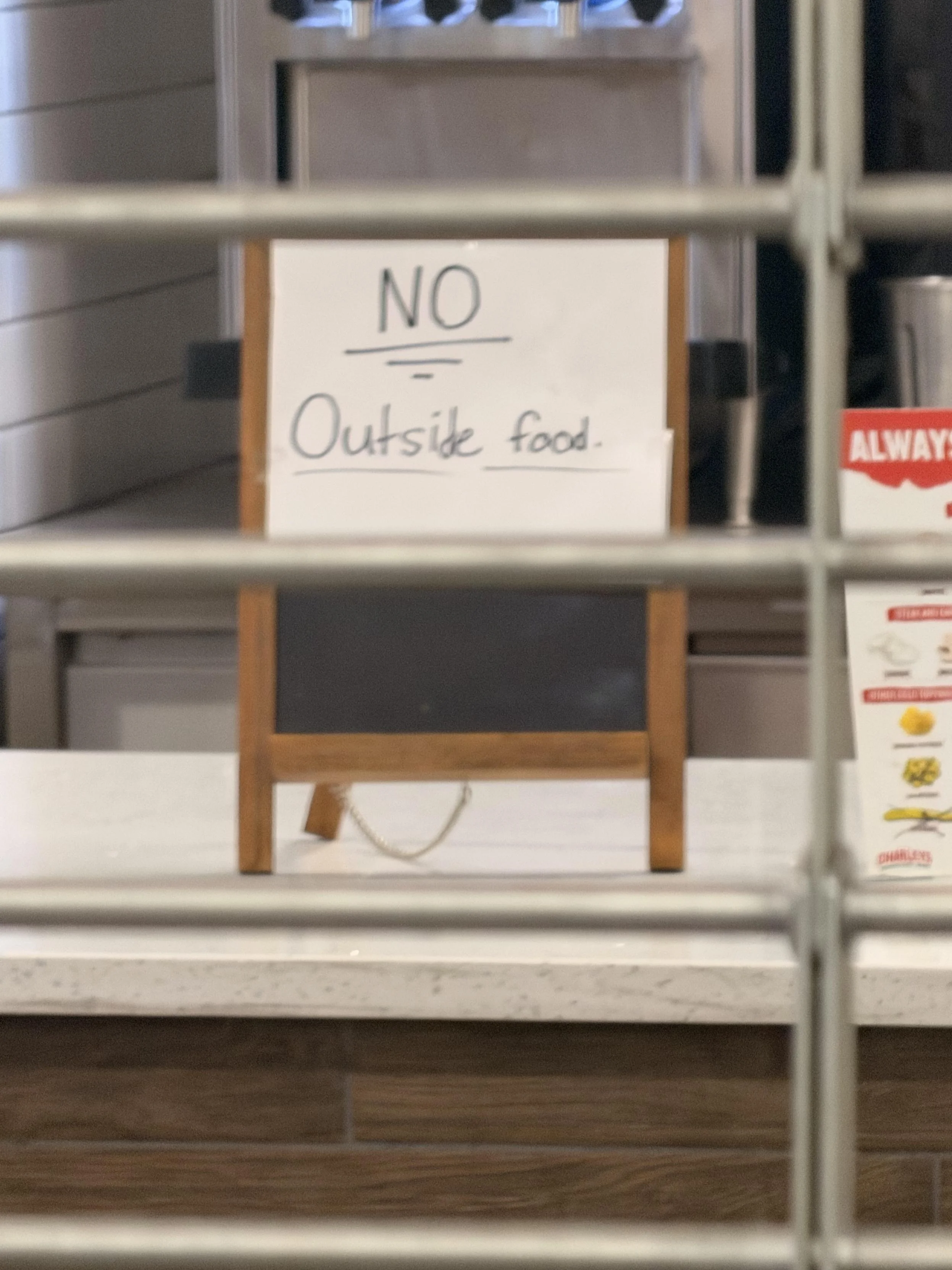 A sign on the other side of a security gate that says “NO OUTSIDE FOOD”